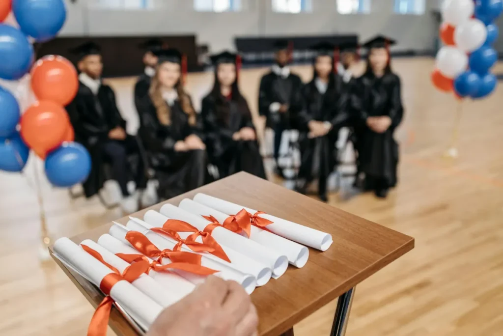 Upacara kelulusan dengan siswa berseragam, dekorasi balon, dan ijazah di atas meja