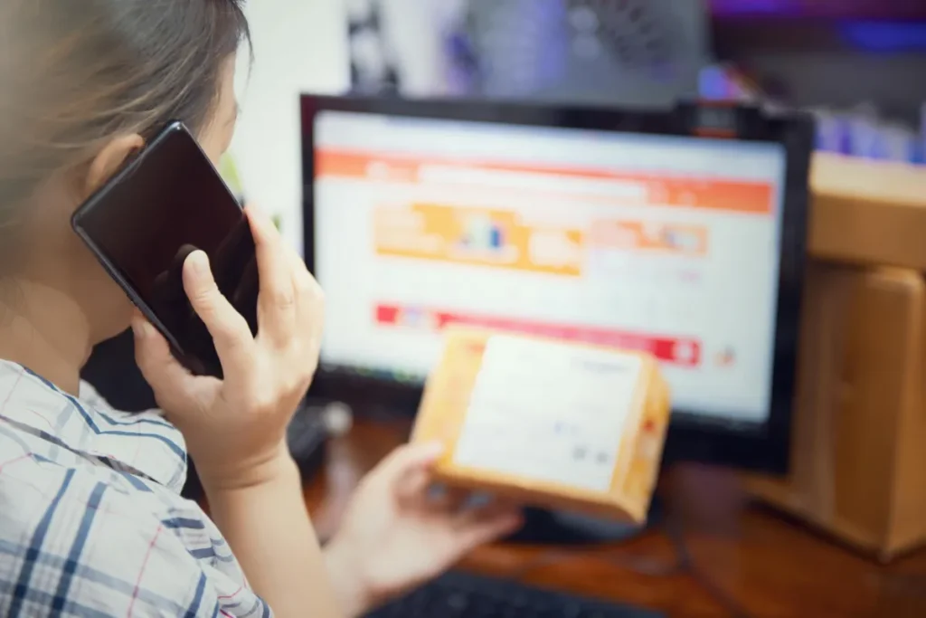 Seorang perempuan menggunakan ponsel sambil memeriksa paket belanja online yang baru diterima